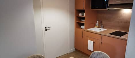 Una cocina compacta con microondas, lavamanos y armarios de madera. Hay una mesa de comedor con dos sillas.