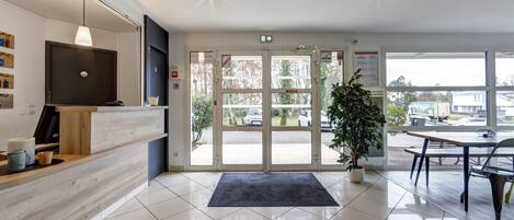 Modtagelsesområde med en trædisk, et fjernsyn, en potteplante og udsigt til parkeringspladsen gennem glasdøre.