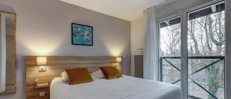 Une chambre moderne avec un grand lit, deux lampes de chevet, une œuvre d’art accrochée au mur et une vue dégagée sur l’extérieur grâce à une grande fenêtre.