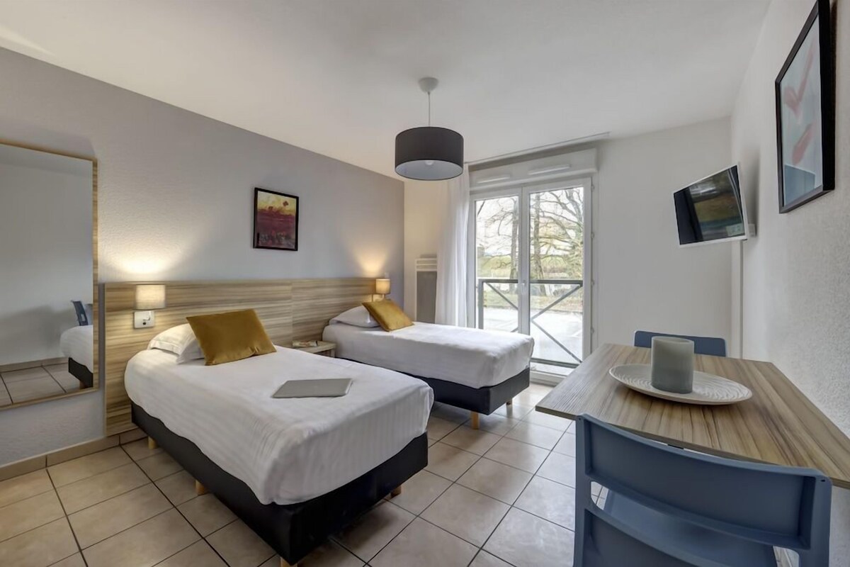 Habitación de hotel con dos camas, un escritorio y un ventanal grande.