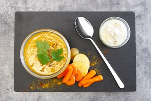 Lasipurkki täynnä appelsiinimausteista dippikastiketta, jonka päällä on persiljaa, sekä lusikka ja porkkanatikkuja liitutaulun päällä.