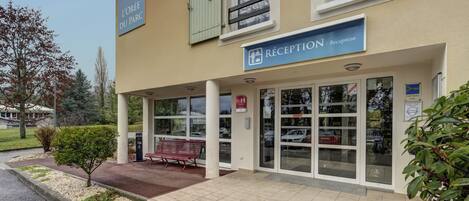 A building with a reception area, a bench, and a sign indicating 'L'ORÉE DU PARC'.