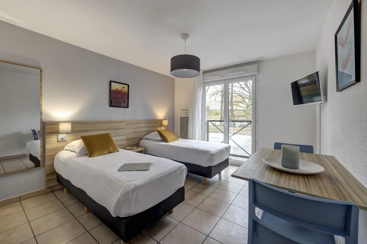 Hotellihuone, jossa on kaksi sänkyä, puinen pöytä, tuoli, televisio ja ikkuna, josta on näkymä.