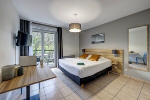 Una habitación de hotel moderna con cama, escritorio con computadora portátil, televisión y balcón con mobiliario exterior.