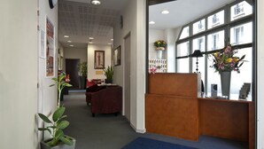 Een receptiegedeelte met een balie, een blauwe mat, planten in potten en ingelijste foto's aan de muur.