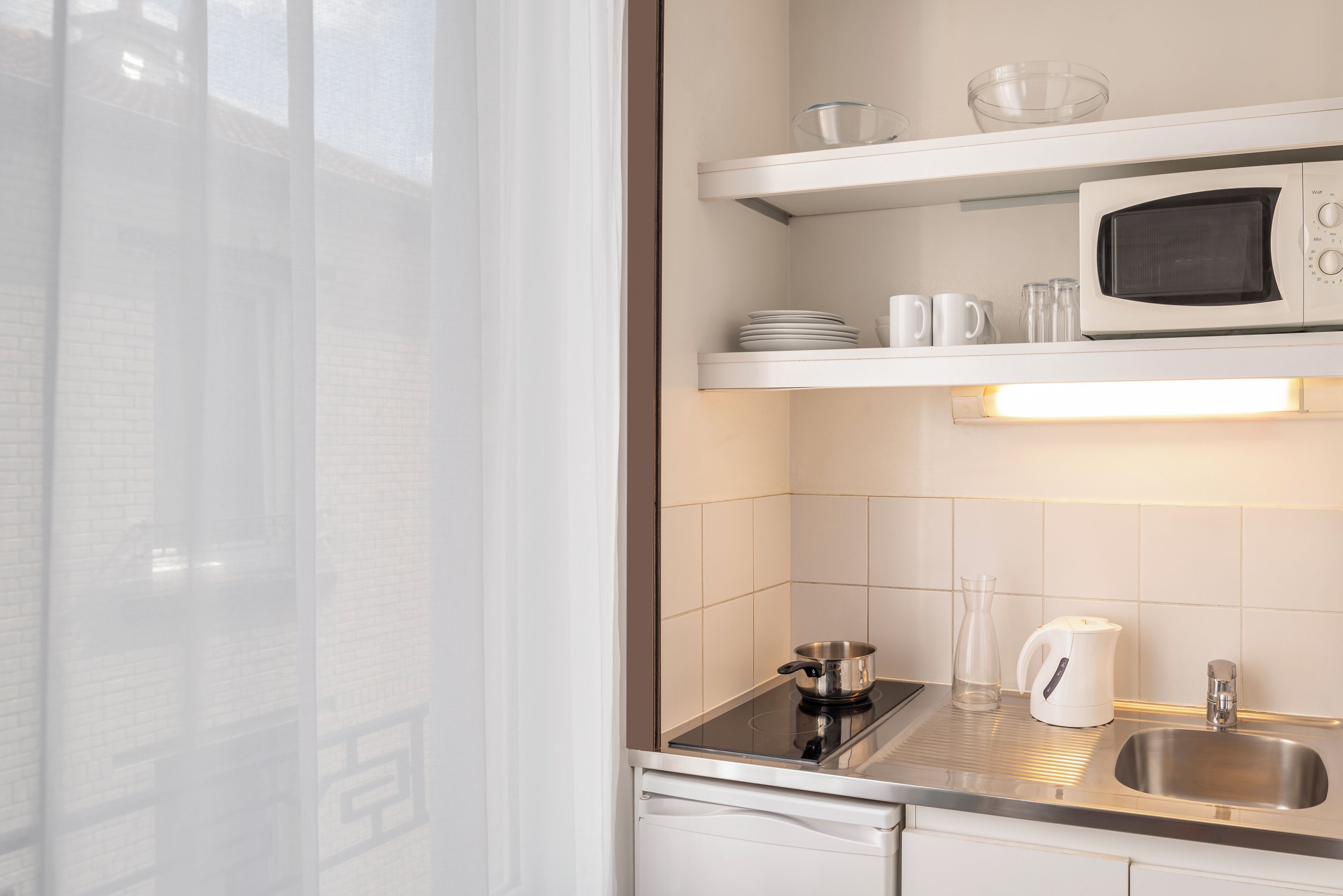 A modern kitchen with white cabinets, a stainless steel sink, a microwave, and a glass pitcher on the countertop.