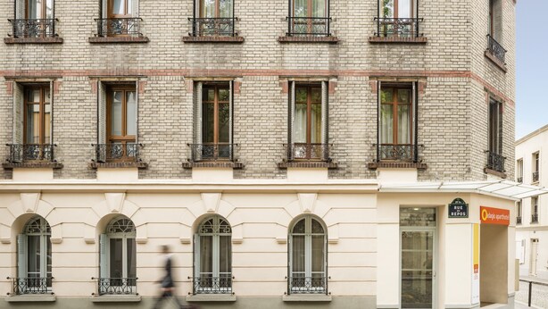 Een meerlaags gebouw in klassieke stijl, met rondboogvensters en balkons voorzien van metalen hekwerk.
