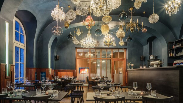 Un restaurante con varias mesas y sillas, una zona de bar y una variedad de candelabros.