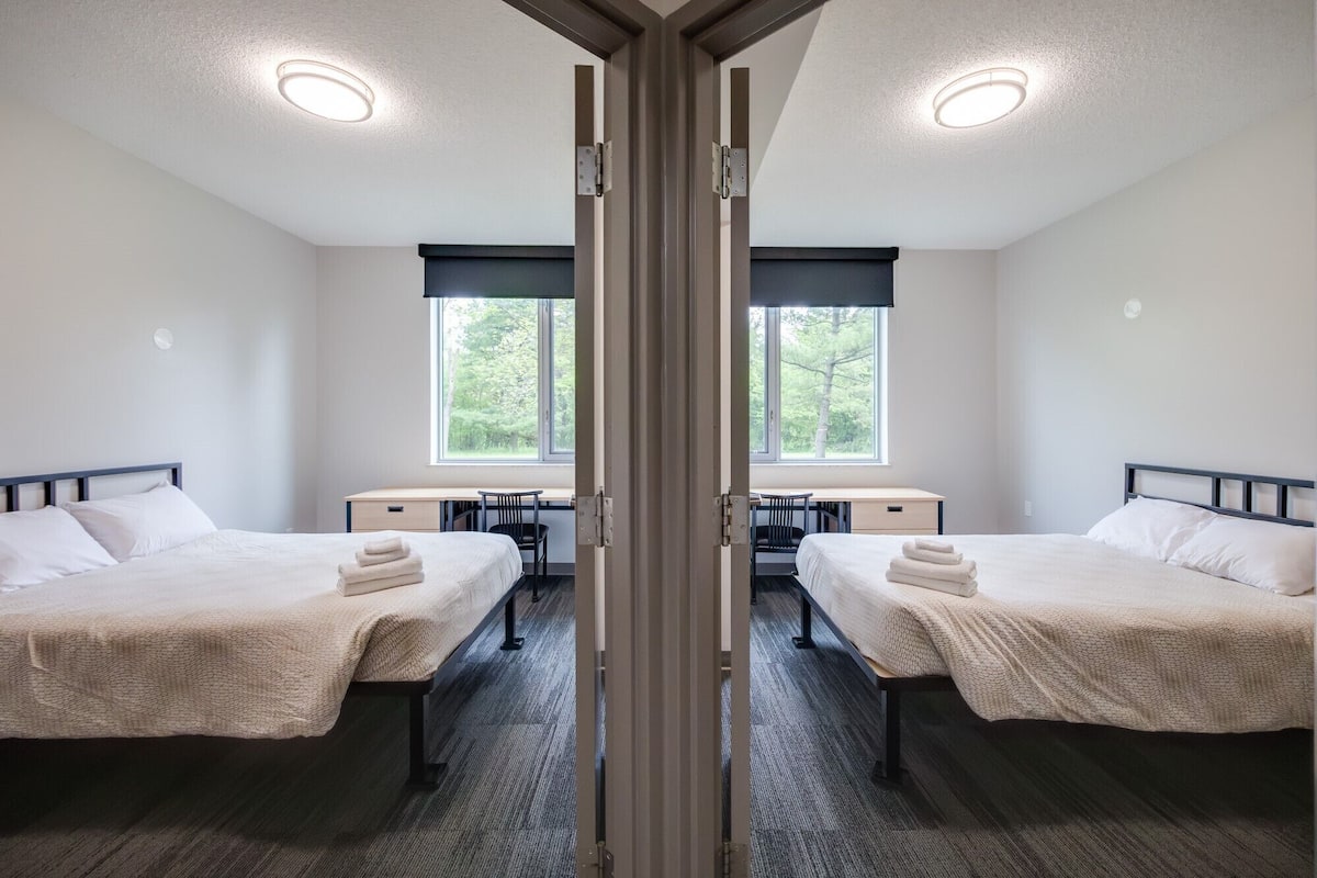 A hotel room with two beds, a desk, and a chair.