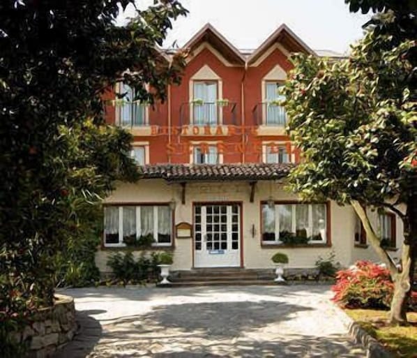 A two-story building with a red facade, a tiled roof, and a central entrance with a door and windows.