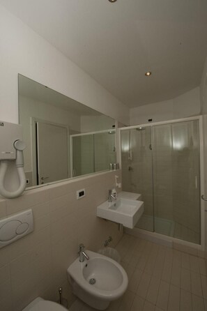 A modern bathroom with a glass-enclosed shower, a bidet, and a sink.