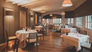 Um restaurante com mesas redondas, piso de madeira e iluminação pendente.