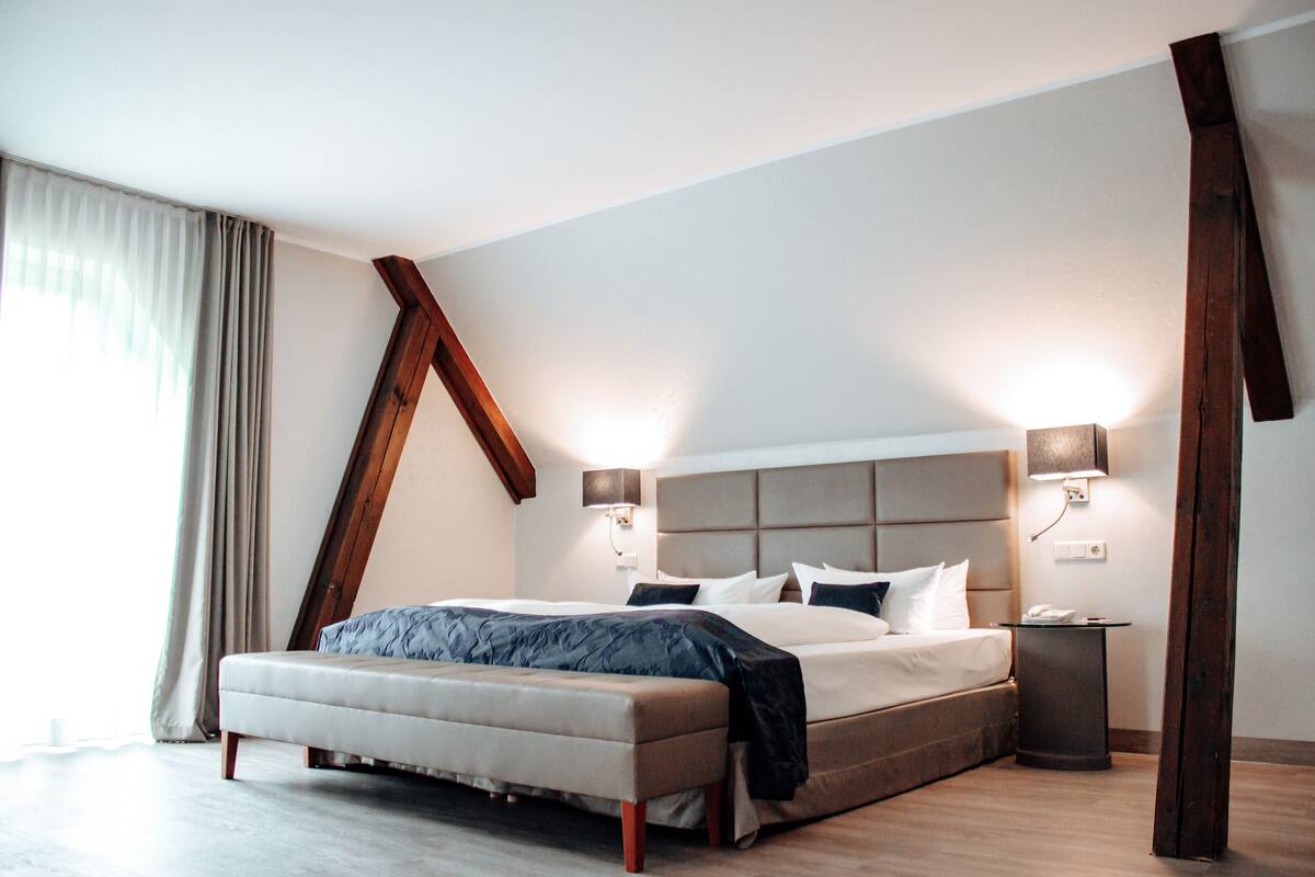 Ein modernes Schlafzimmer mit einem großen Bett, einer Bank, zwei Nachttischen und einer schrägen Decke.