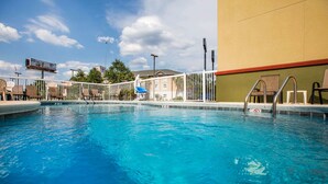 A swimming pool with a white fence, lounge chairs, and a building in the background. - Econo Lodge Valdosta Mall Area (Valdosta)