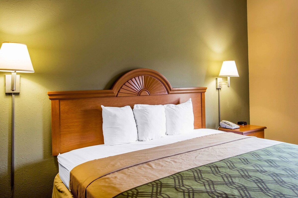 A hotel room with a wooden headboard, a bed with white bedding, two bedside lamps, and a telephone on the nightstand.