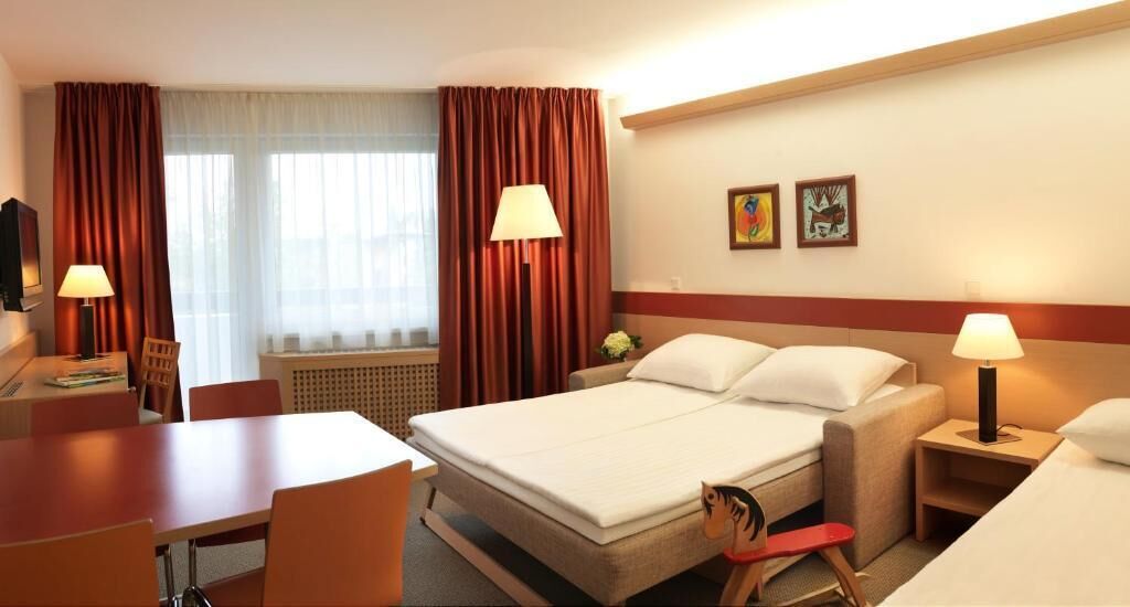 A hotel room with a bed, two bedside tables, a desk, a chair, and a window with curtains.