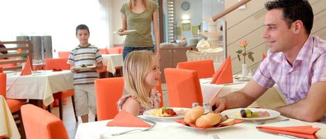 A family dining in a restaurant with orange chairs and white tablecloths.