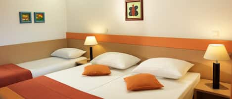 Camera d'albergo con due letti, ognuno con biancheria bianca e cuscini arancioni. Sono presenti due comodini con lampade e un quadro appeso al muro.