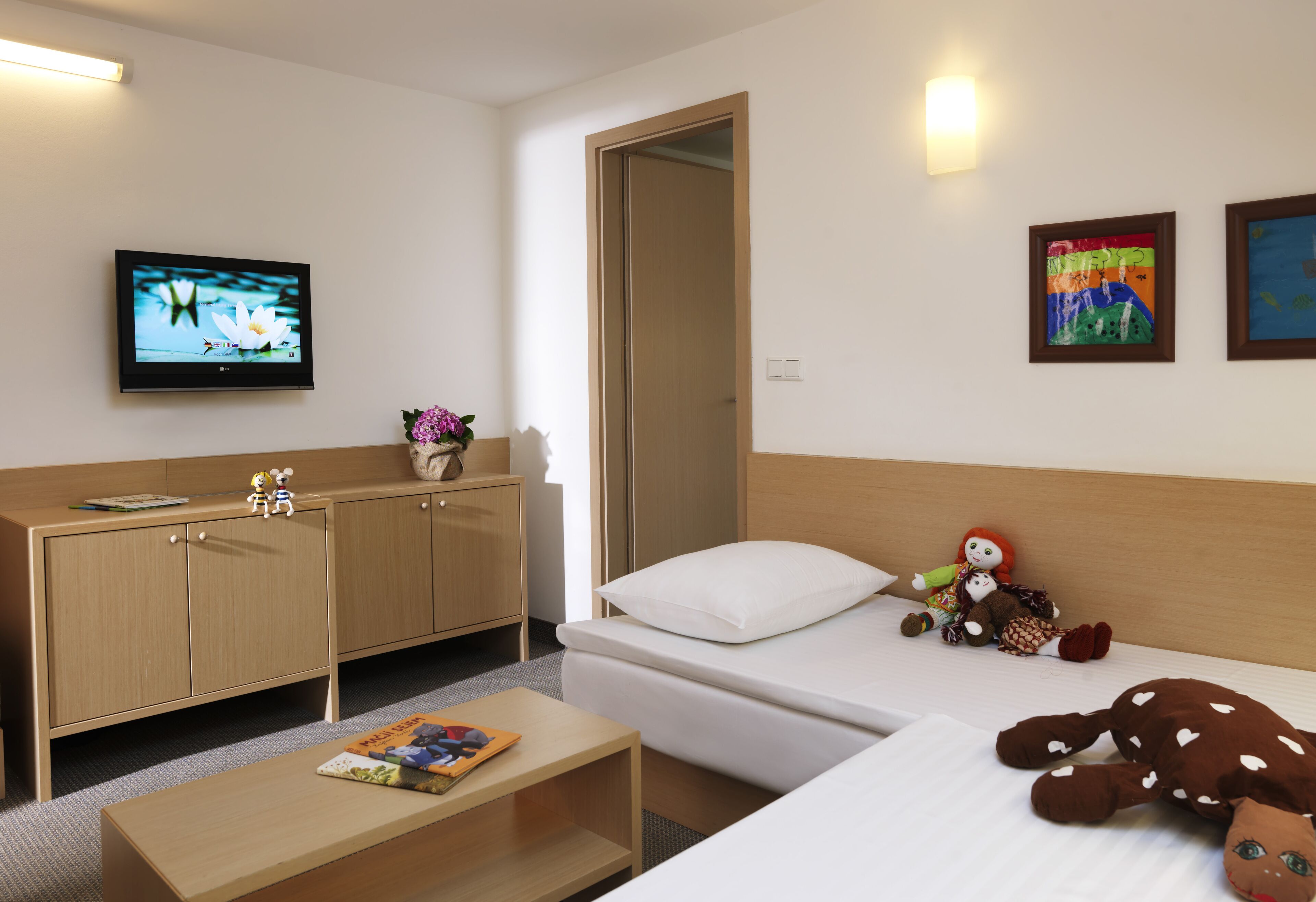 A hotel room with a bed, a desk, a television, and artwork on the walls.
