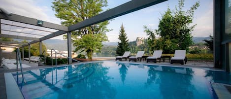 A modern outdoor swimming pool with lounge chairs and a glass enclosure.
