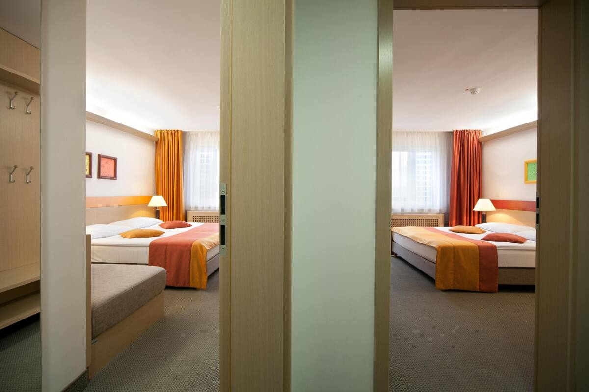 A hotel room with two beds, a wardrobe, a desk, and a window with curtains.