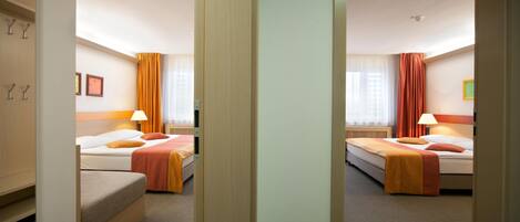 A hotel room with two beds, a wardrobe, a desk, and a window with curtains.