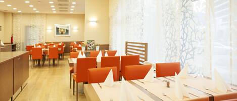 A restaurant with multiple tables and chairs, a wooden counter, and a patterned wall.