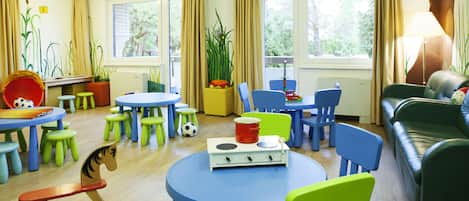 A children's playroom with round tables, colorful chairs, and various toys.
