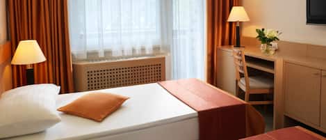 Ett hotellrum med två sängar, ett skrivbord, en stol, en lampa och en tv.