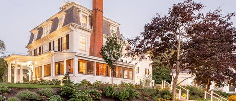 A large, historic house with a prominent chimney, a well-maintained garden, and a staircase leading to the entrance.