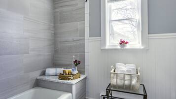 A bathroom with a bathtub, a window with a view, and a shelf with towels and toiletries.
