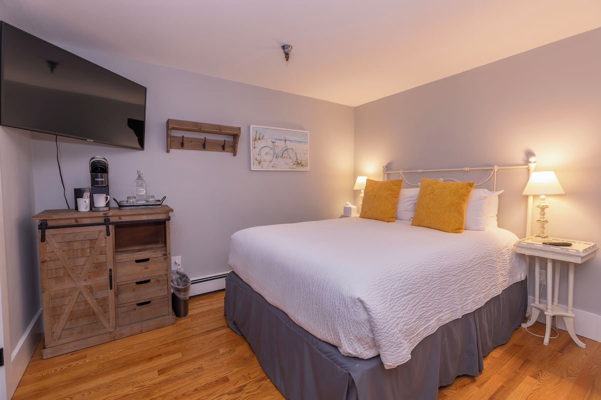 A bedroom with a bed, bedside tables, a TV, a coffee maker, and a wooden cabinet.