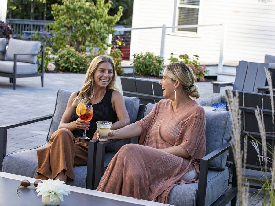 Two people seated on outdoor patio furniture, holding drinks.