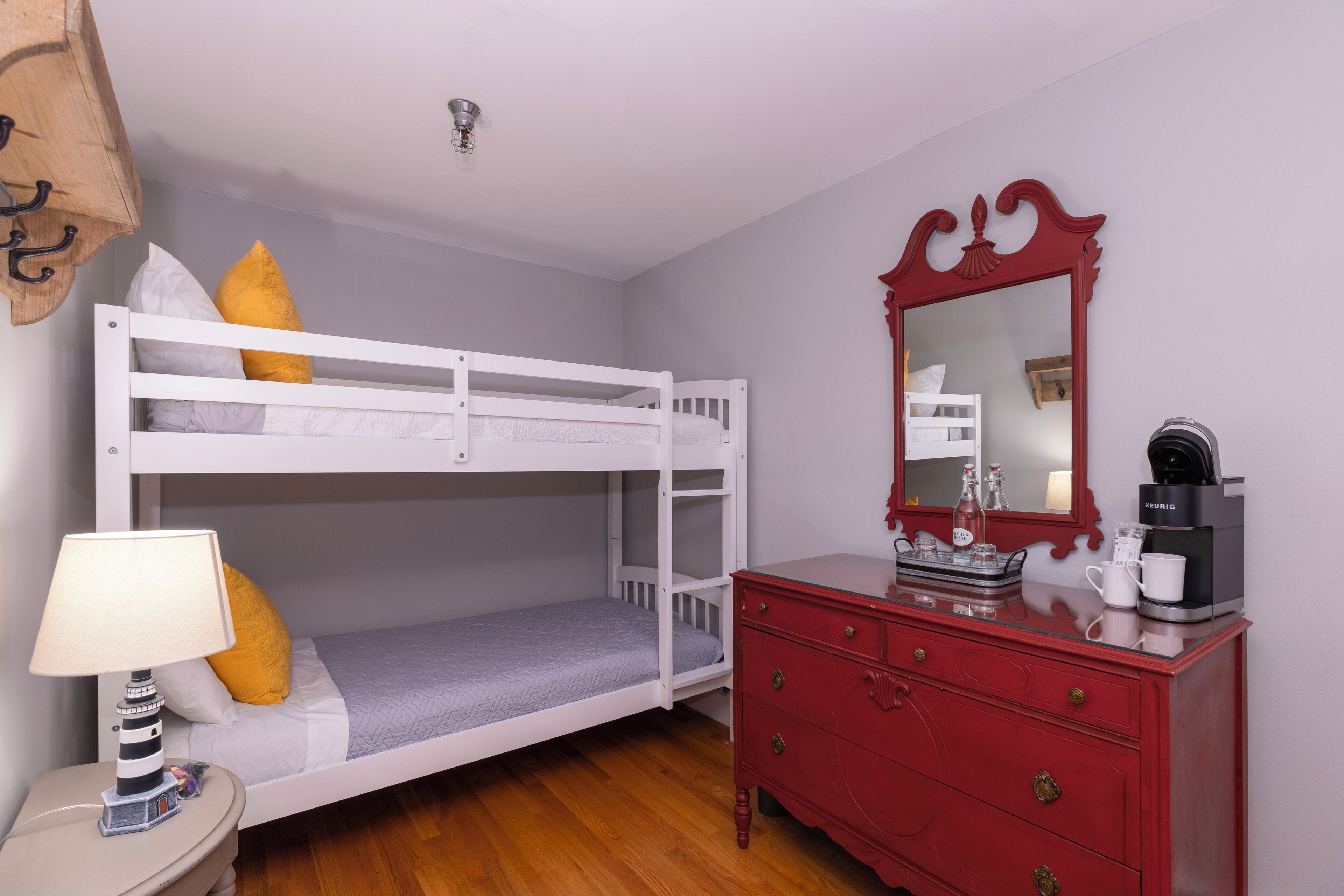 A bunk bed with a white frame, a red dresser with drawers, a lamp, and a mirror with a red frame.