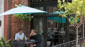 Two people dining at Farm Bell Kitchen, with a menu board displaying meal times and a phone number. - Dinsmore Boutique Inn (Charlottesville)