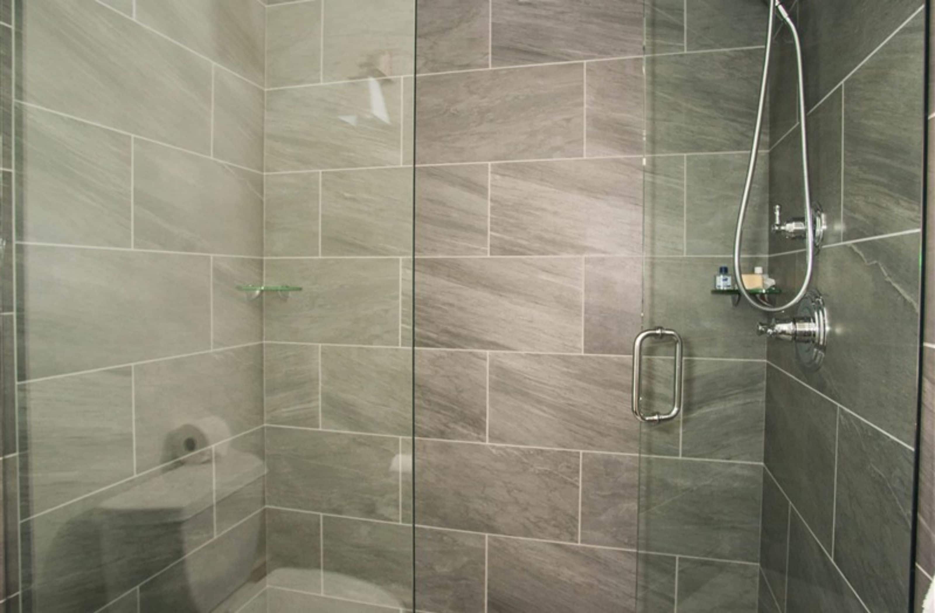 A glass-enclosed shower stall with a handheld showerhead and a glass shelf.