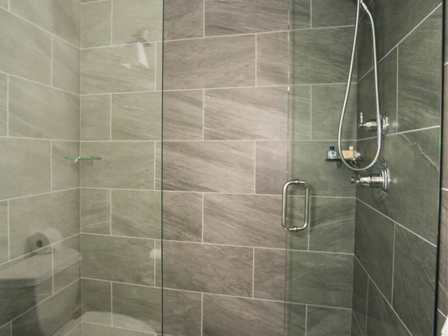 A glass-enclosed shower stall with a handheld showerhead and a glass shelf.