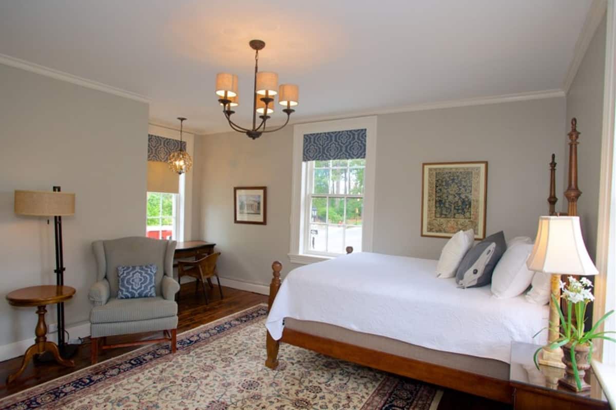 A bedroom with a large bed, a chandelier, a chair, a table, and a window with a view.