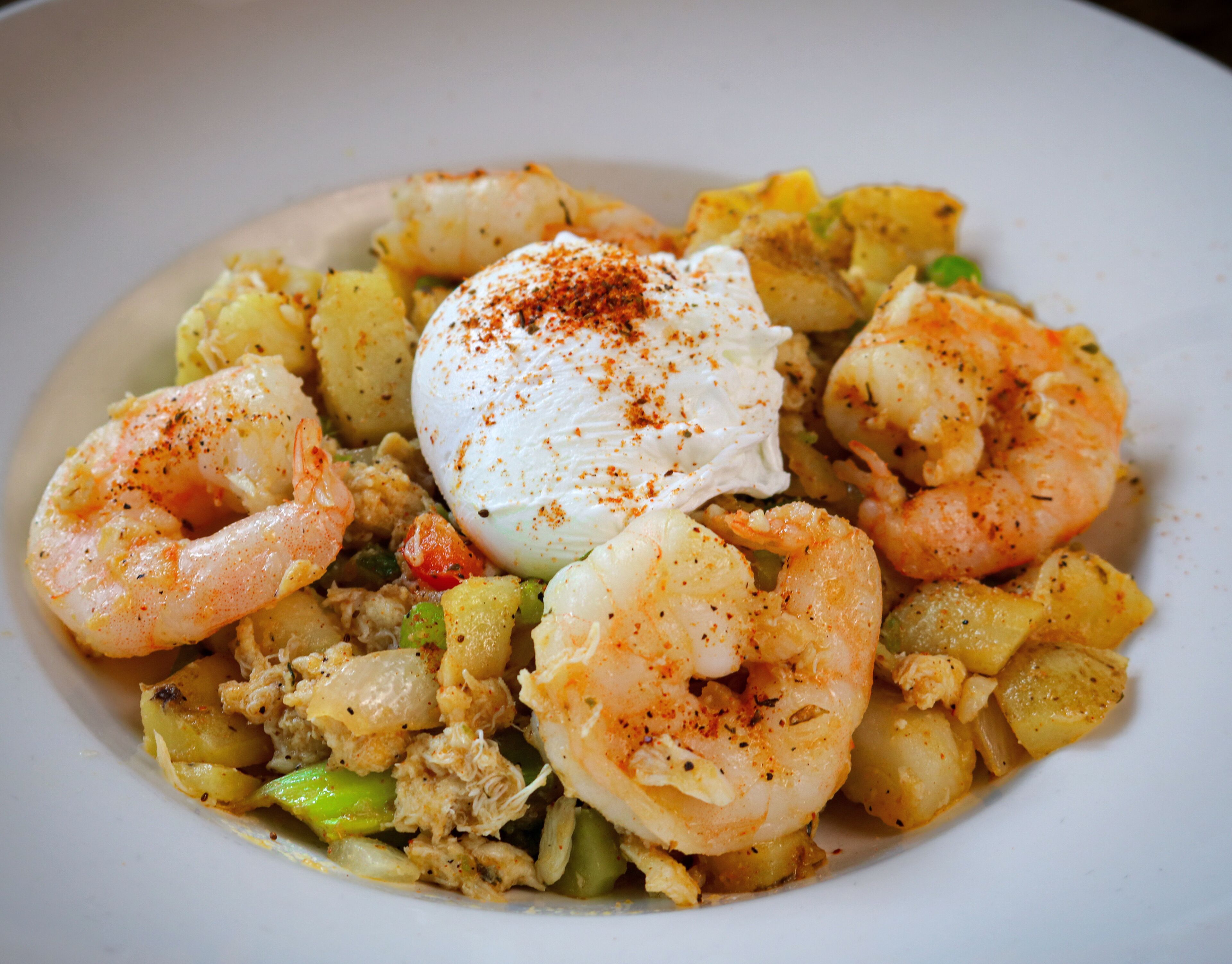 A plate of shrimp and vegetables with a poached egg on top.