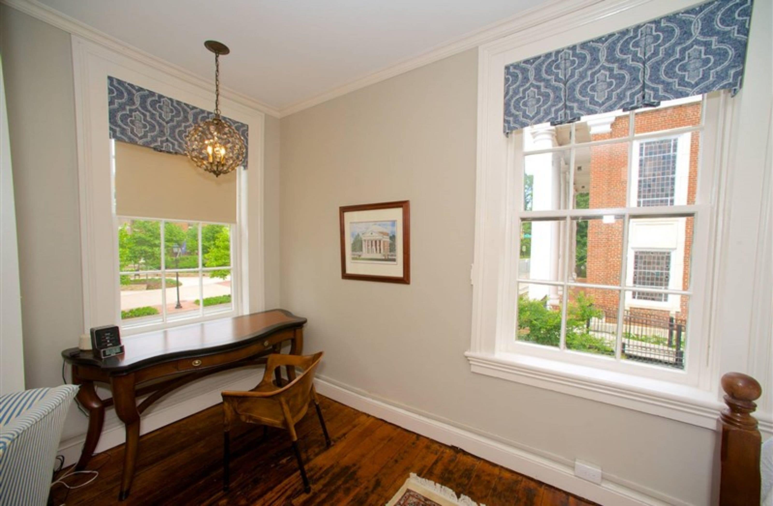 A room with a desk, chair, and a large window with patterned valance.