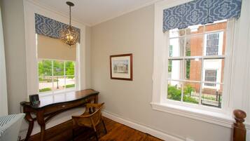 A room with a desk, chair, and a large window with patterned valance.