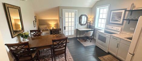 A dining area with a wooden table and chairs, a kitchen with a stove and refrigerator, and a door leading to another room.