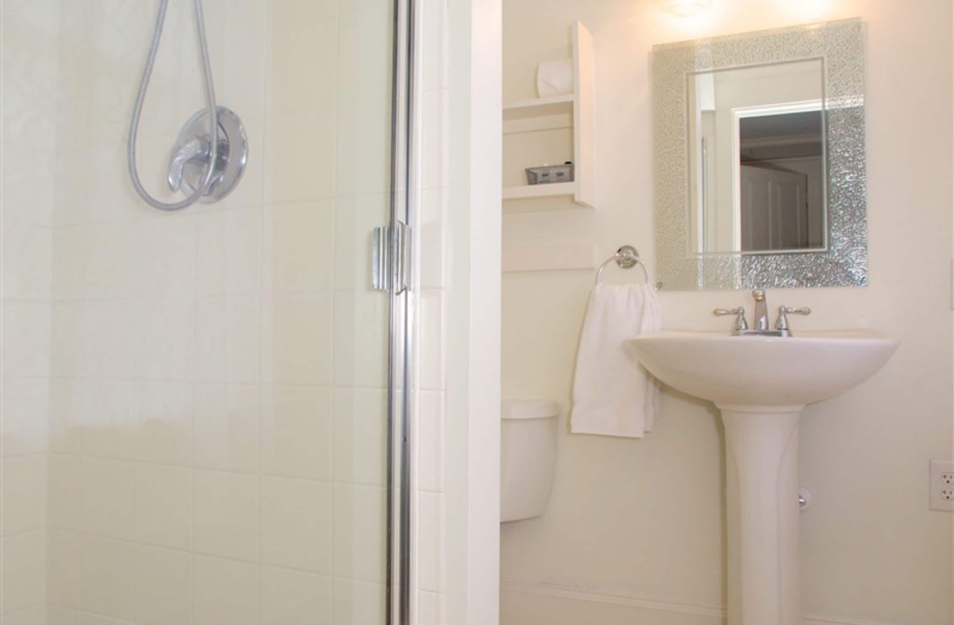 A bathroom with a glass shower enclosure, a white sink, and a mirror with a decorative frame.