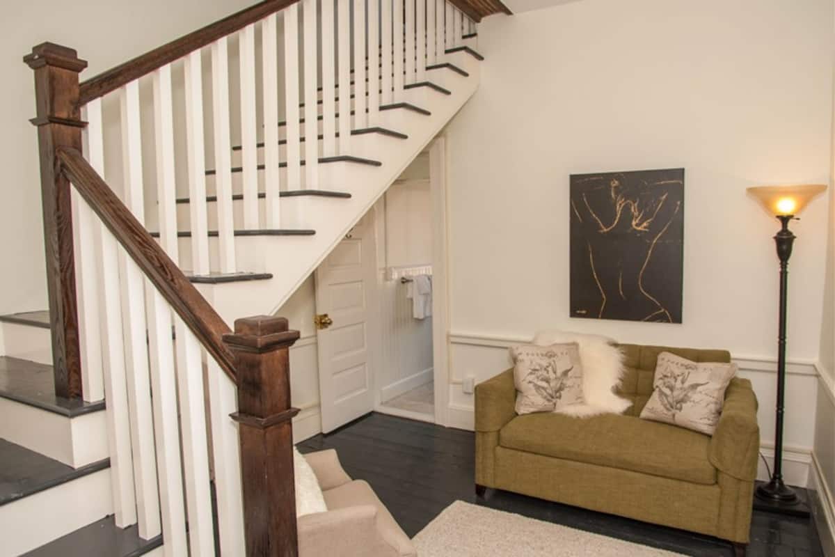 A staircase with wooden railings, a beige sofa with decorative pillows, a floor lamp, and a piece of abstract art on the wall.