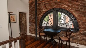 A room with a brick wall, a large arched window, wooden flooring, and a table with chairs. - Dinsmore Boutique Inn (Charlottesville)