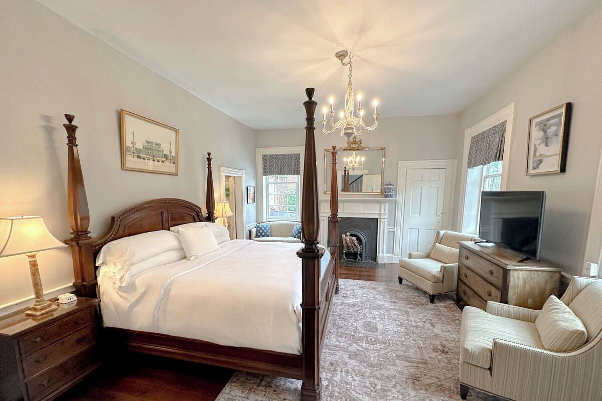 A spacious bedroom with a large bed, a sitting area with a TV, and a fireplace.