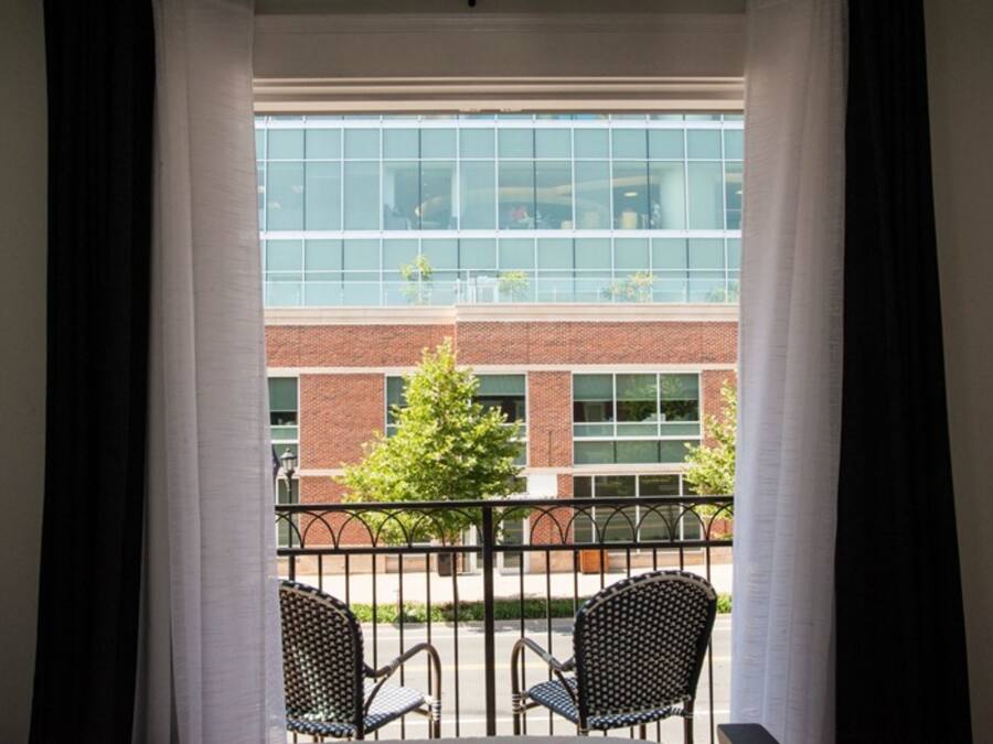 A room with a view of a brick building and a tree through a window with black curtains.