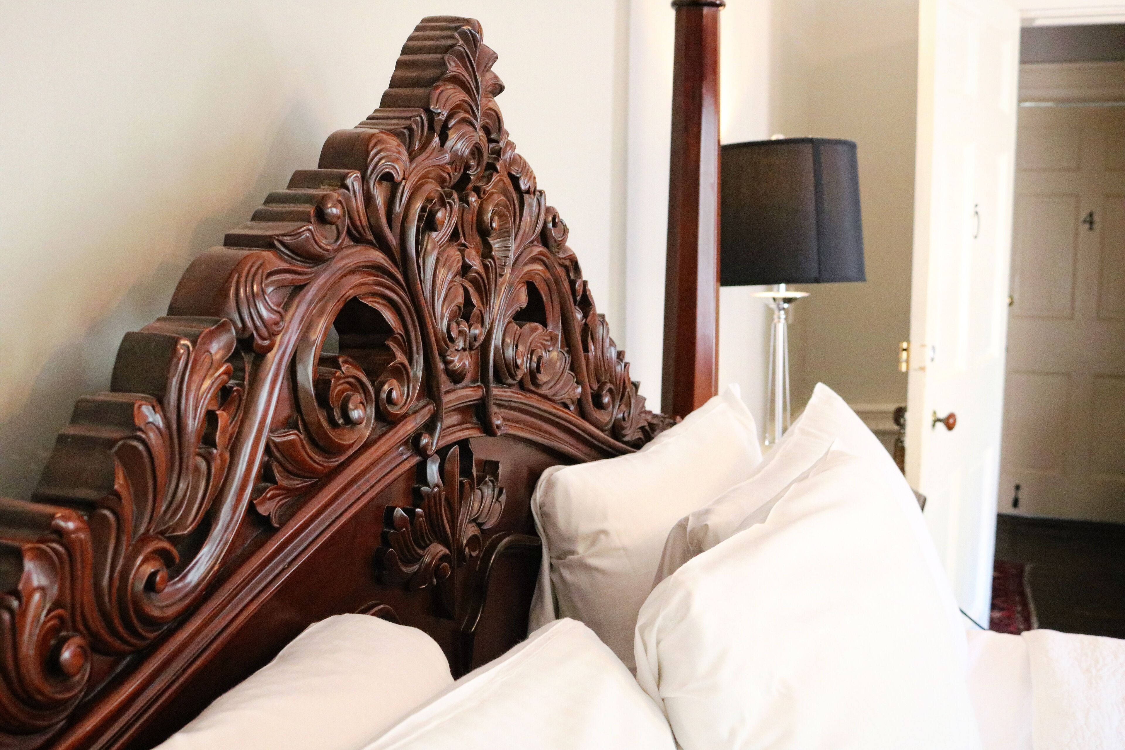 A bedroom with an ornate wooden headboard, a bedside lamp, and white bedding.