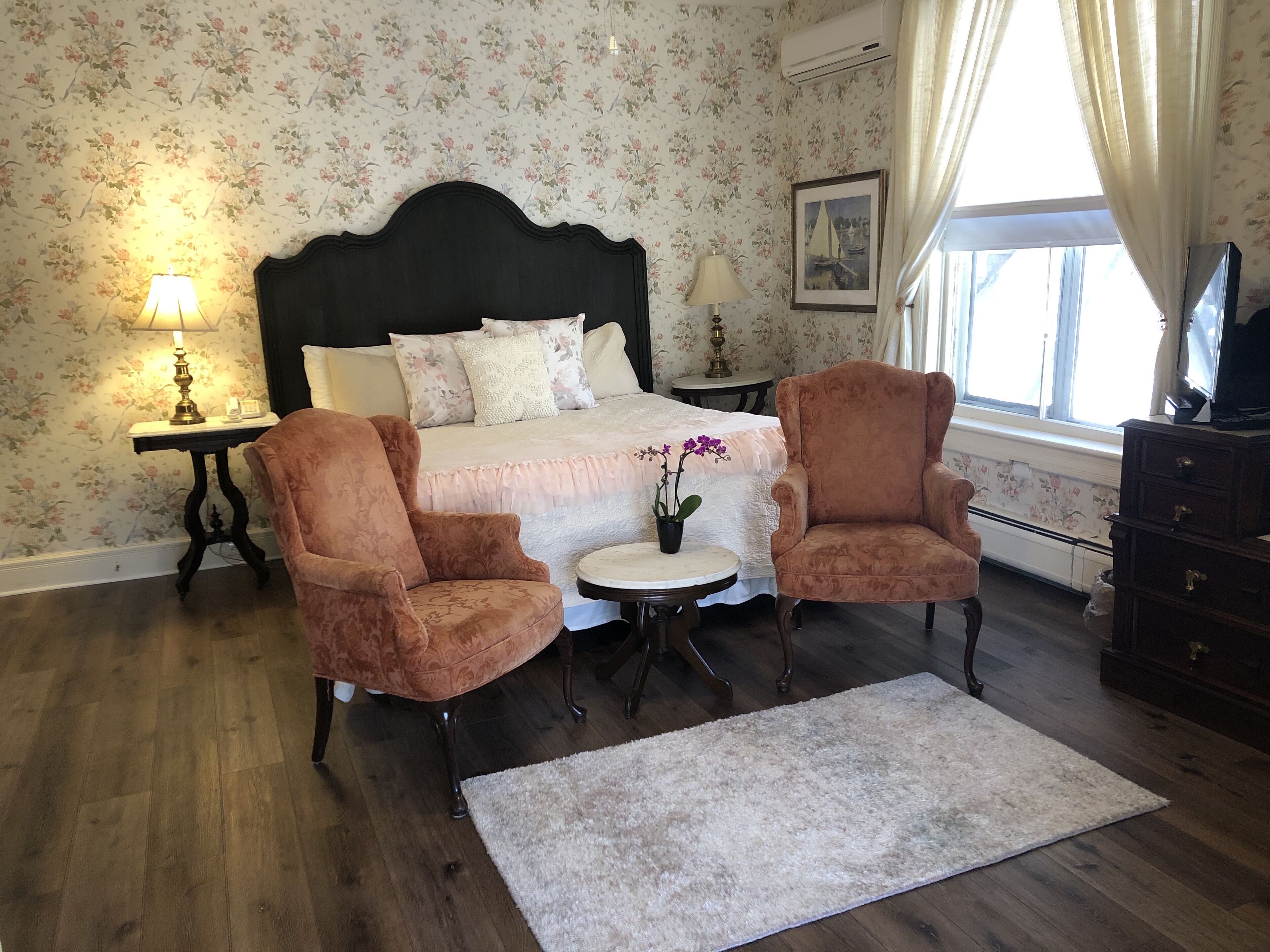 A bedroom with a large bed, two armchairs, a small table, and a nightstand with lamps.