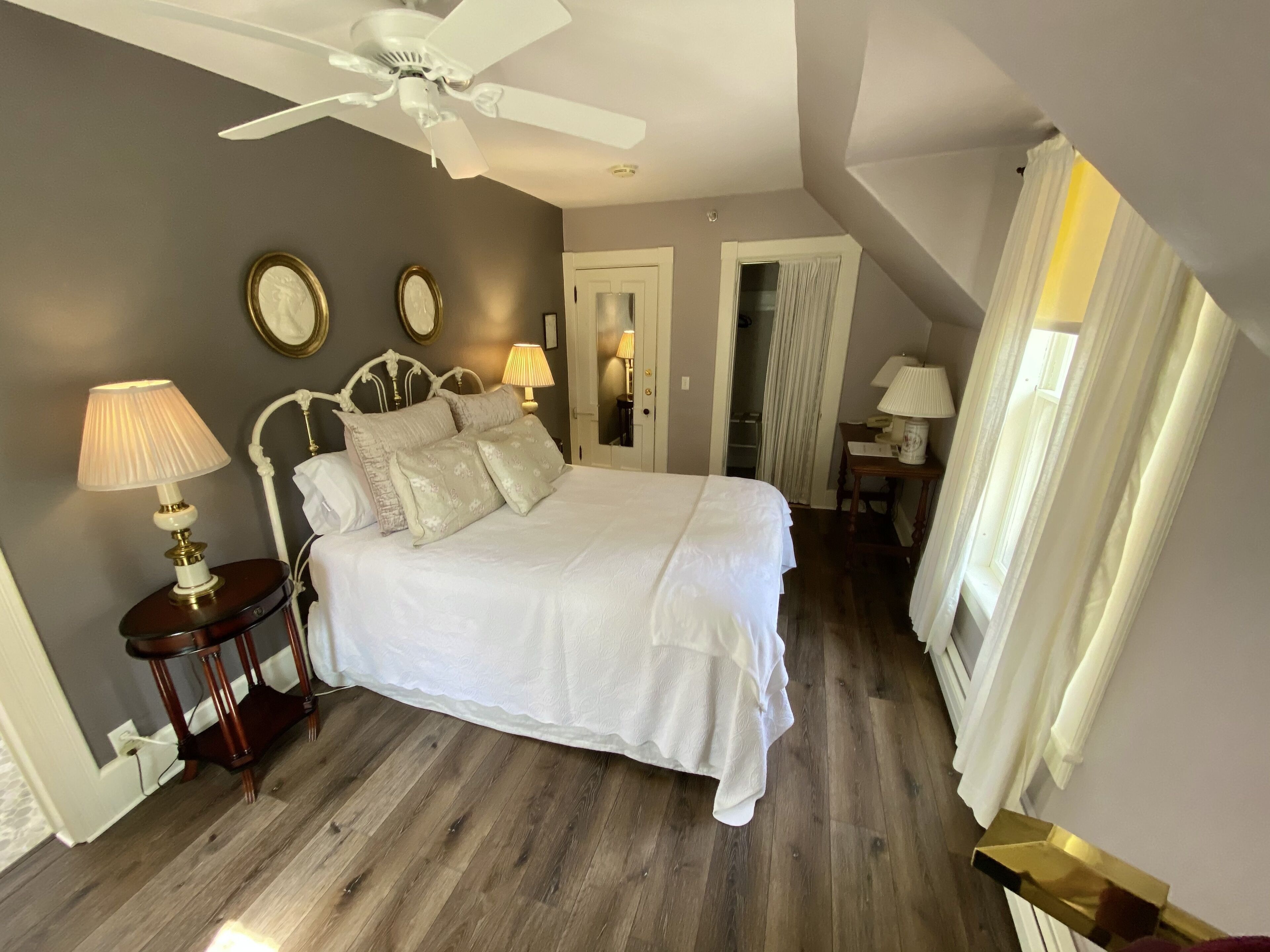 A bedroom with a large bed, a ceiling fan, and a nightstand with a lamp.